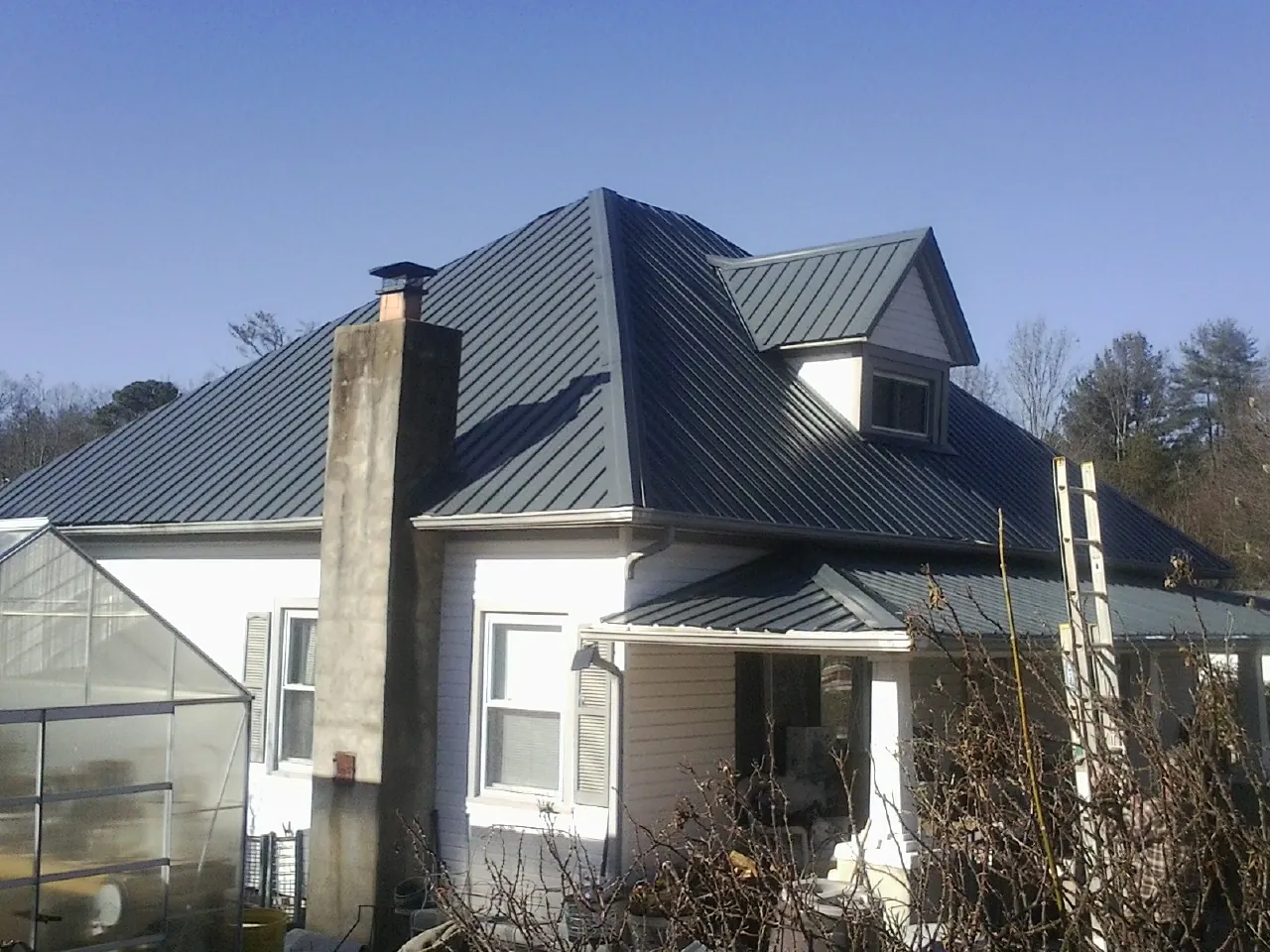 Dark blue standing seam metal roof on a white farmhouse with dormer — Slate & Tile Roof Repair by Roofing Brothers in Scottsbluff