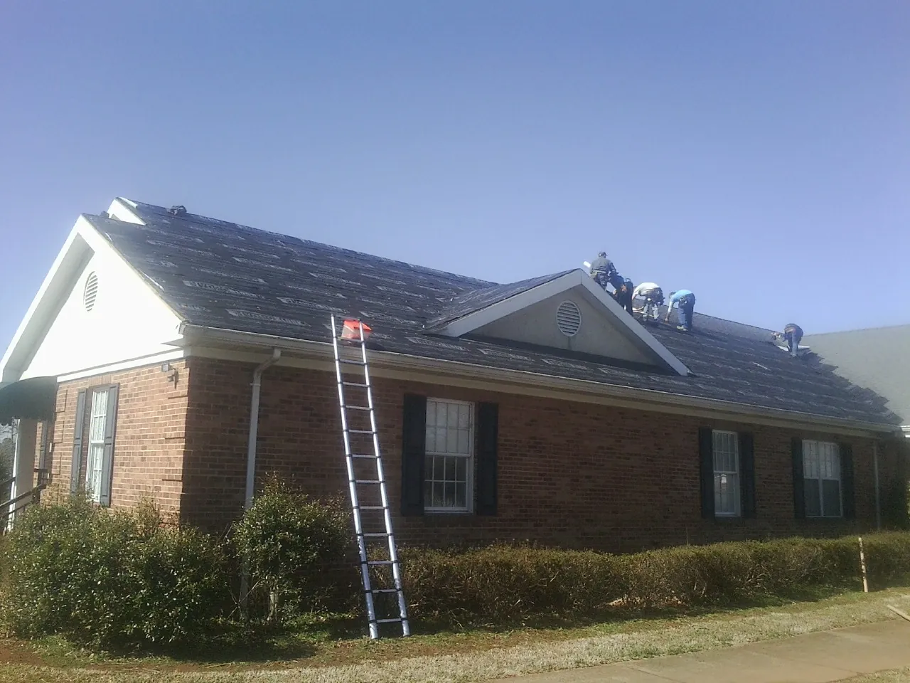 Crew tearing shingles off a brick ranch roof with a ladder set — Metal Roof Repair work by our crew in Scottsbluff