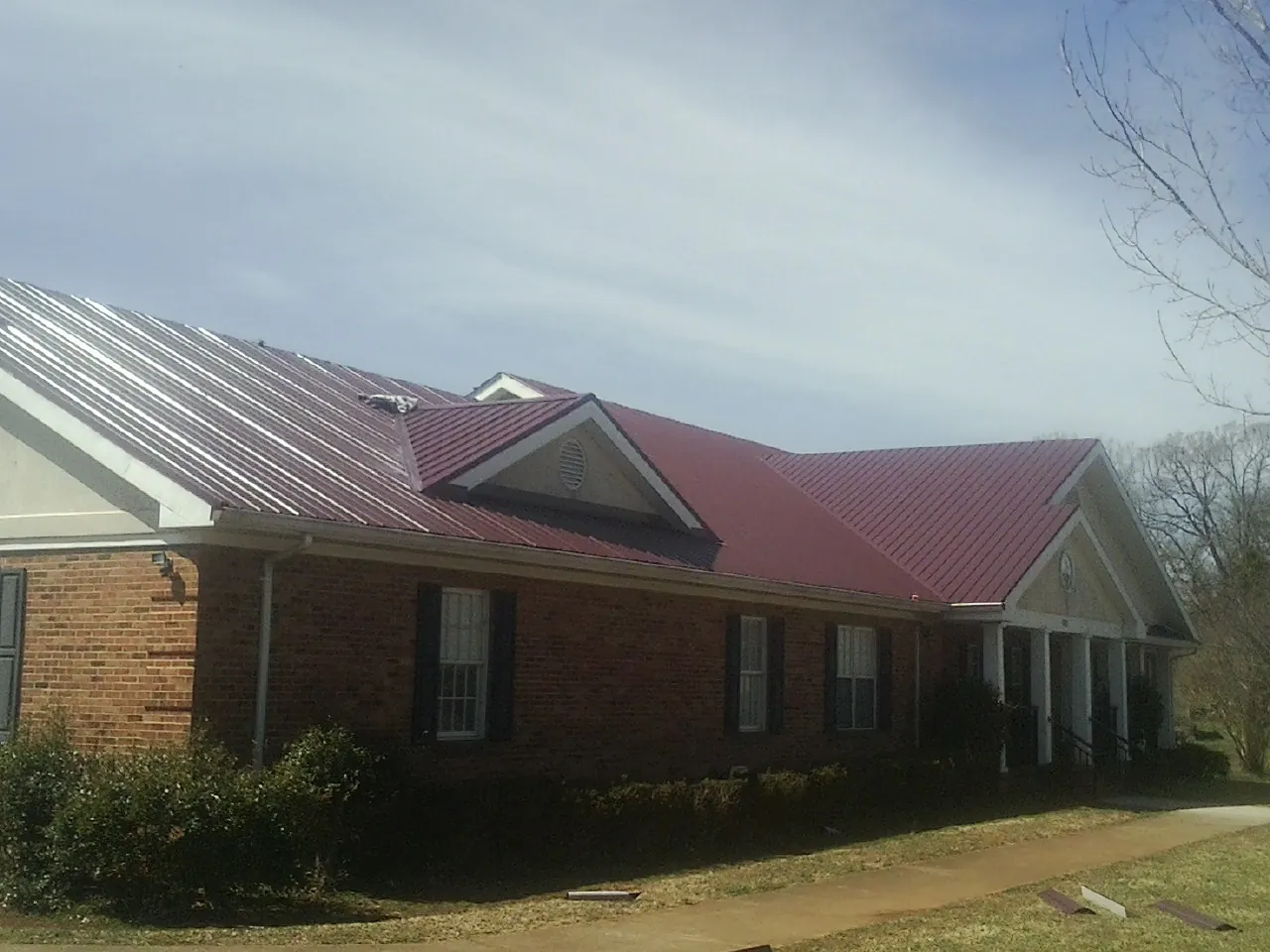 Red metal roof with gabled entries on a long brick building, from a Hail Damage Roof Repair job in Scottsbluff