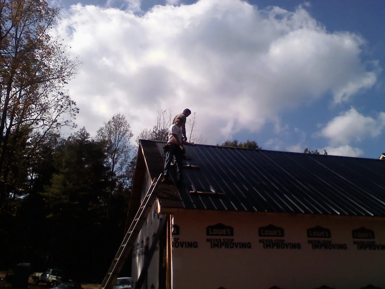 Roofer fastening dark metal panels high against a cloudy sky, from a Roof Inspection job in Scottsbluff