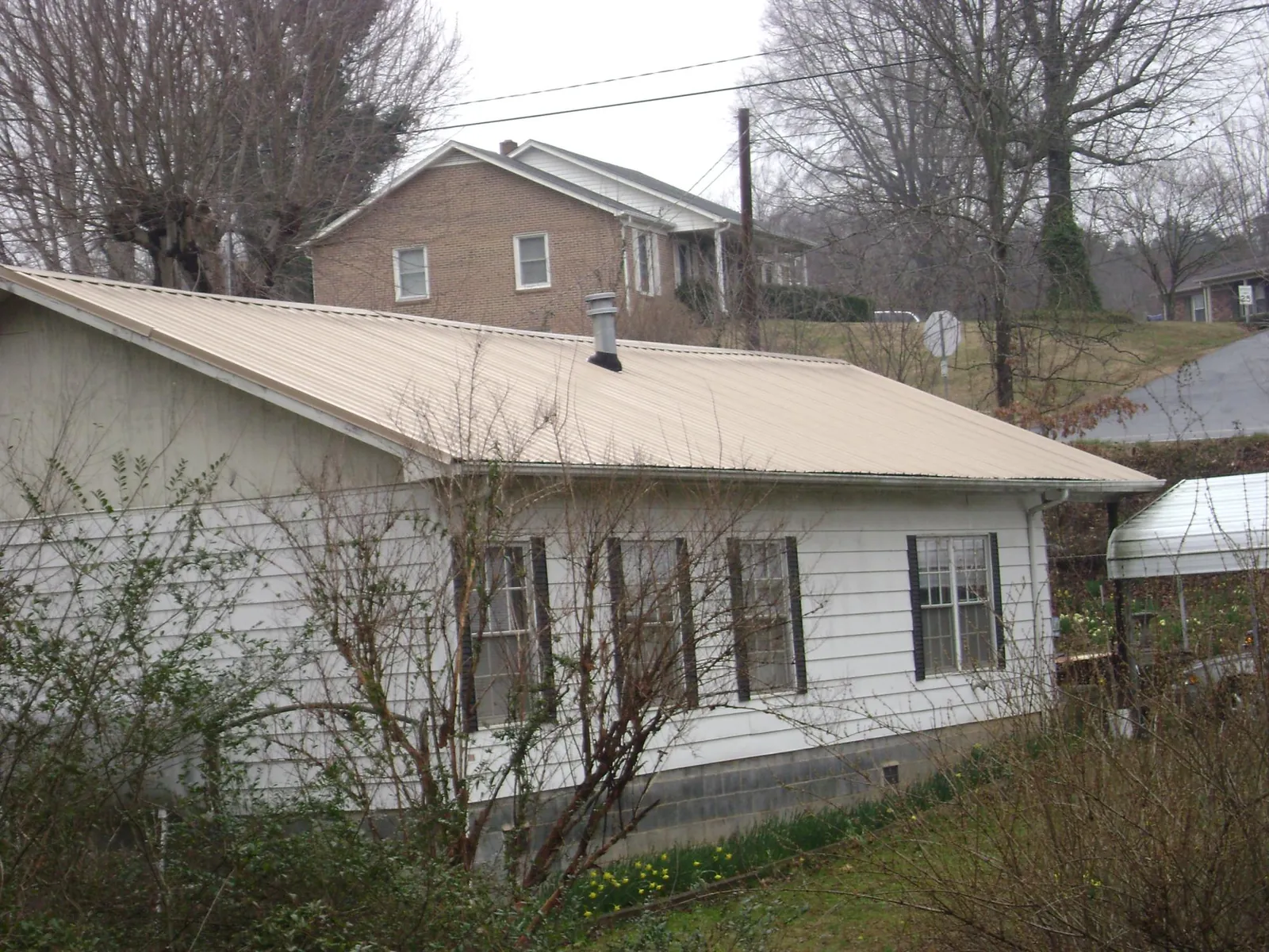 Tan metal roof on a white sided house set into a hillside — Commercial Roofing by Roofing Brothers in Scottsbluff